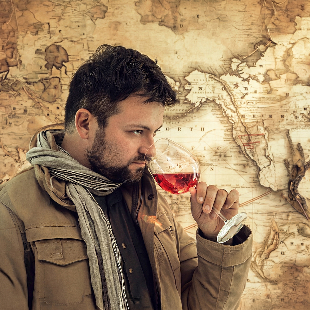 Michele Bean enologo Roi Clar assaggia un bicchiere di vino rosso con una mappa antica dell'Europa alle sue spalle